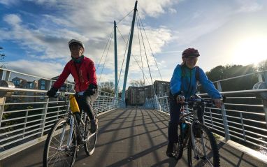 Two women cycling over the Millennium Bridge at Lancaster Wildey Media